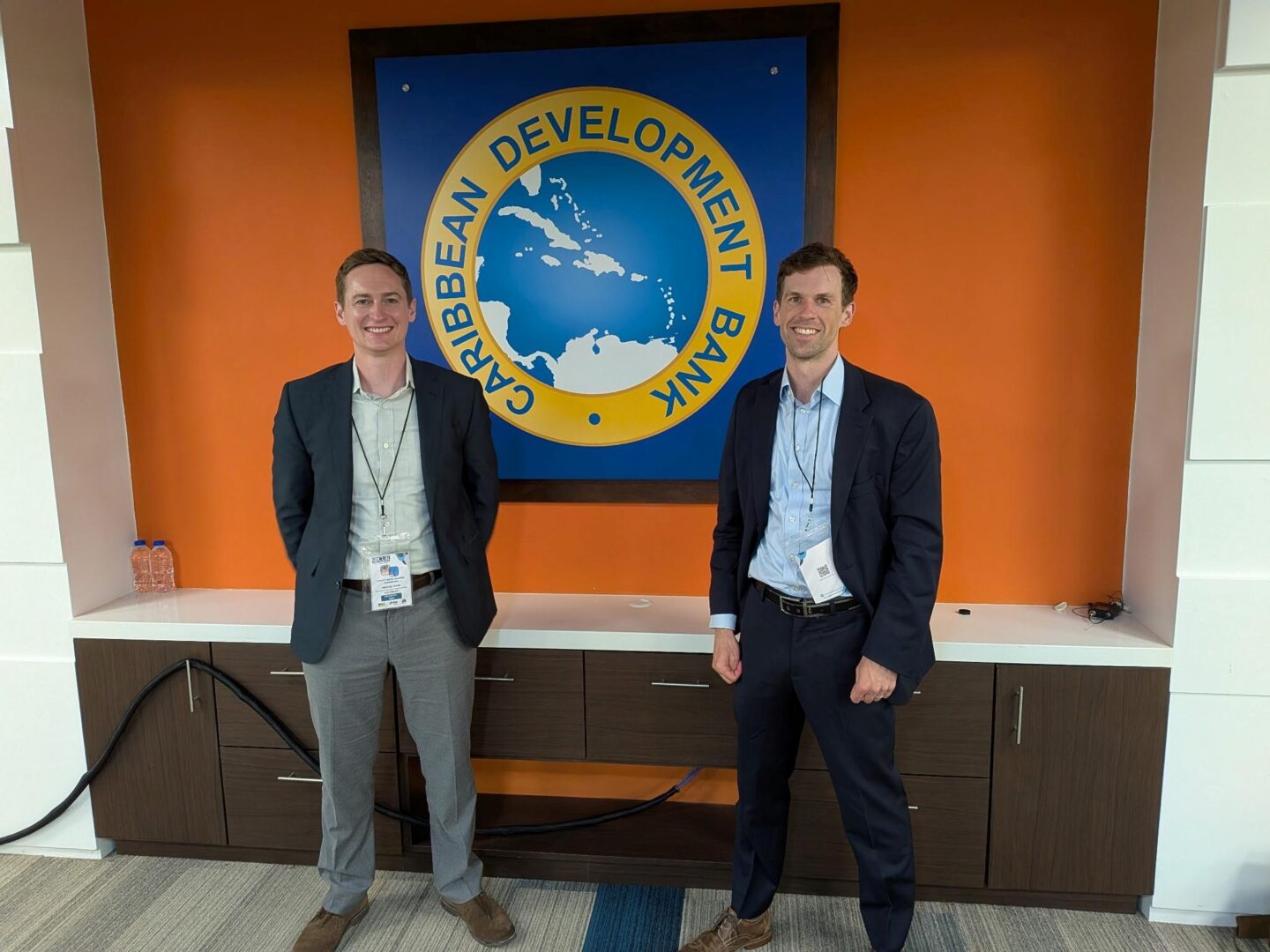 Nick and Mike stand in front of the Caribbean Development Bank seal